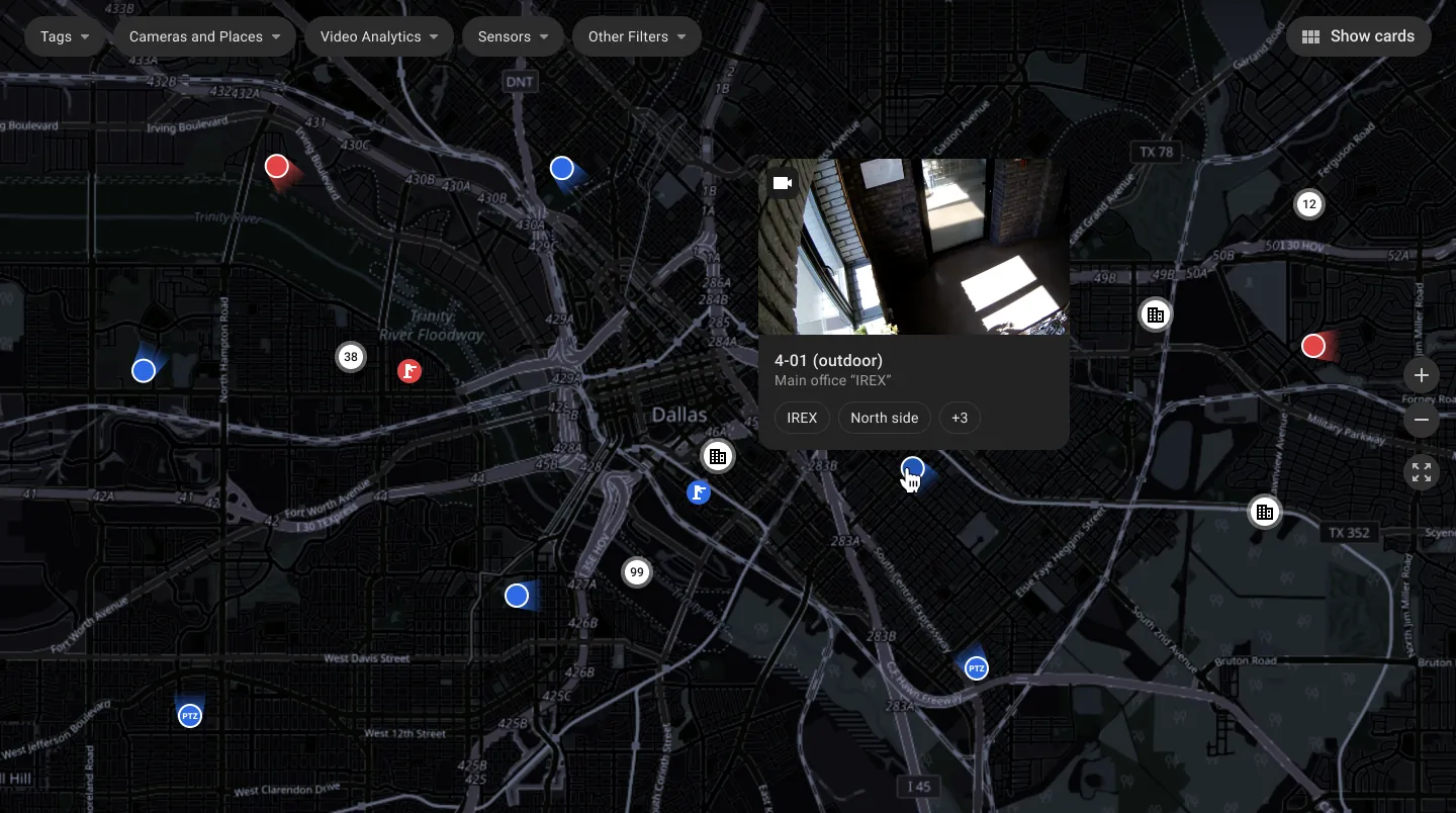 A dark city-scale IREX map of Dallas: camera pins showing view direction, cluster badges reading 38, 99 and 12, building and map-mark icons and a live-preview pop-up from camera 4-01 (outdoor) at the IREX main office with its tags