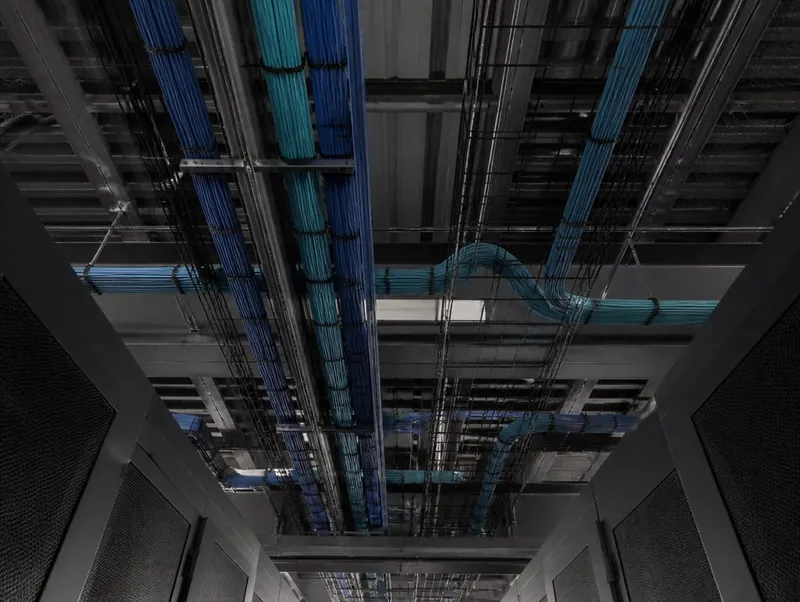 The ceiling of a data hall seen from directly below: separate cable bundles running along overhead trays and branching away over the aisles