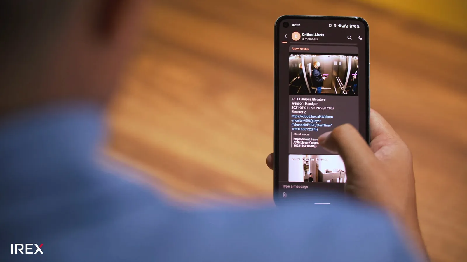 A responder holding a phone showing a Sover critical-alerts channel, where the alarm notifier has posted a weapon-detection frame with the camera name, the weapon class, the timestamp and a playback link
